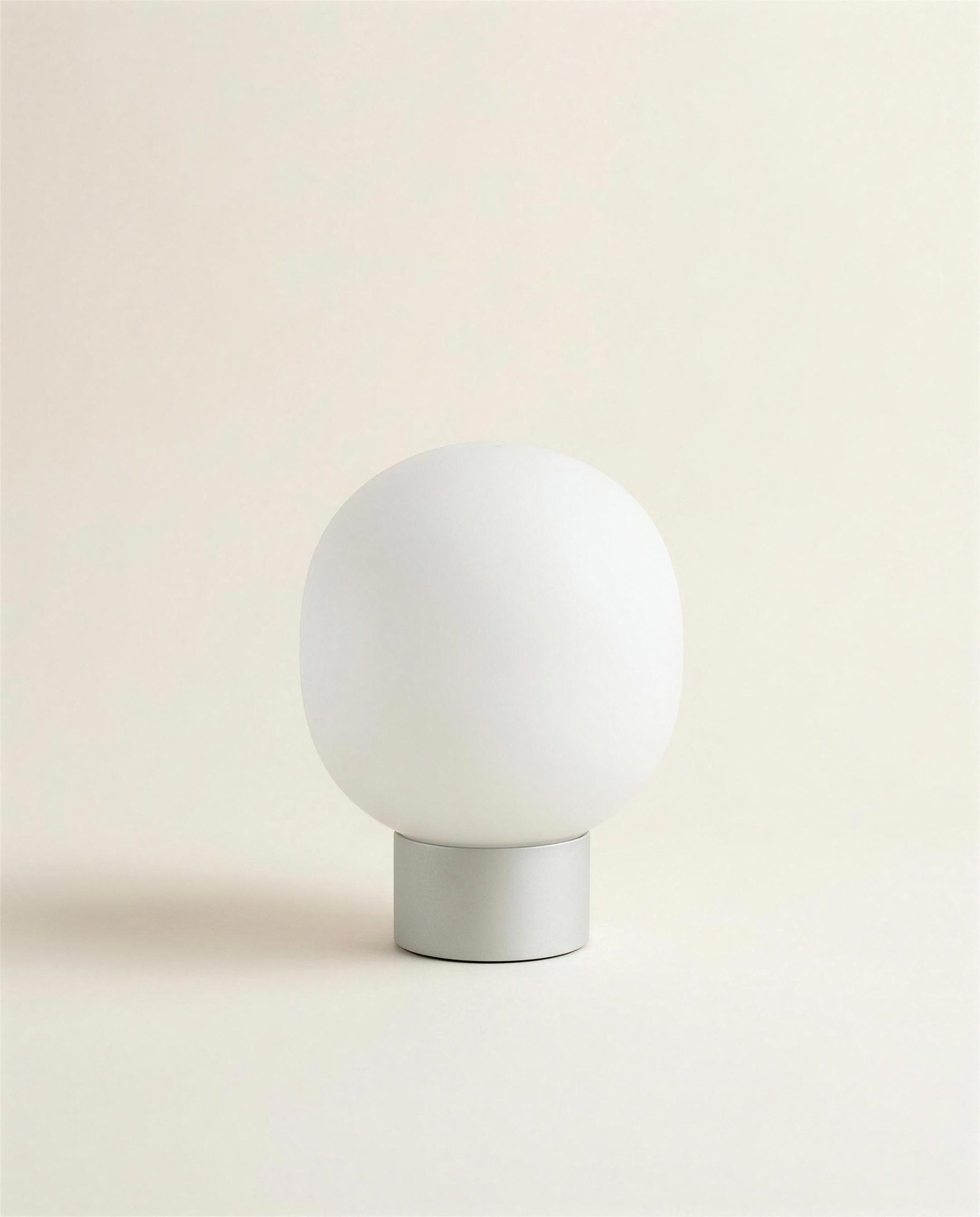 The Fen Table Light: a rounded hand-blown opal glass globe seated on a short machined pale grey base.
