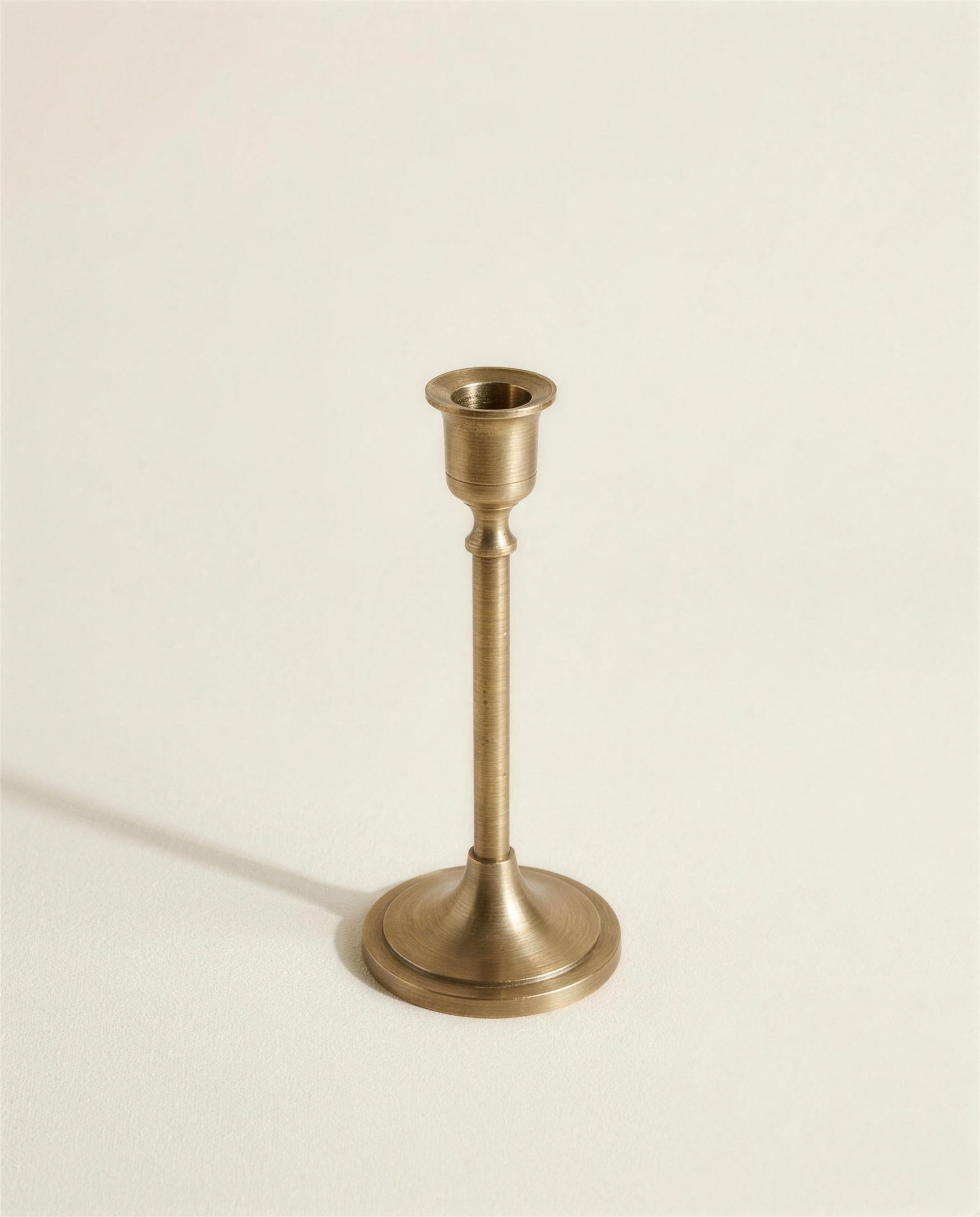 The Stave Candlestick: a slim turned brass column on a weighted round foot with an empty candle cup.